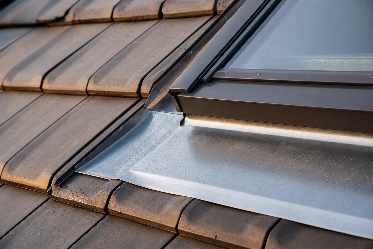 Raccord d’étanchéité en zinc autour d’une fenêtre de toit neuve sur couverture en tuiles